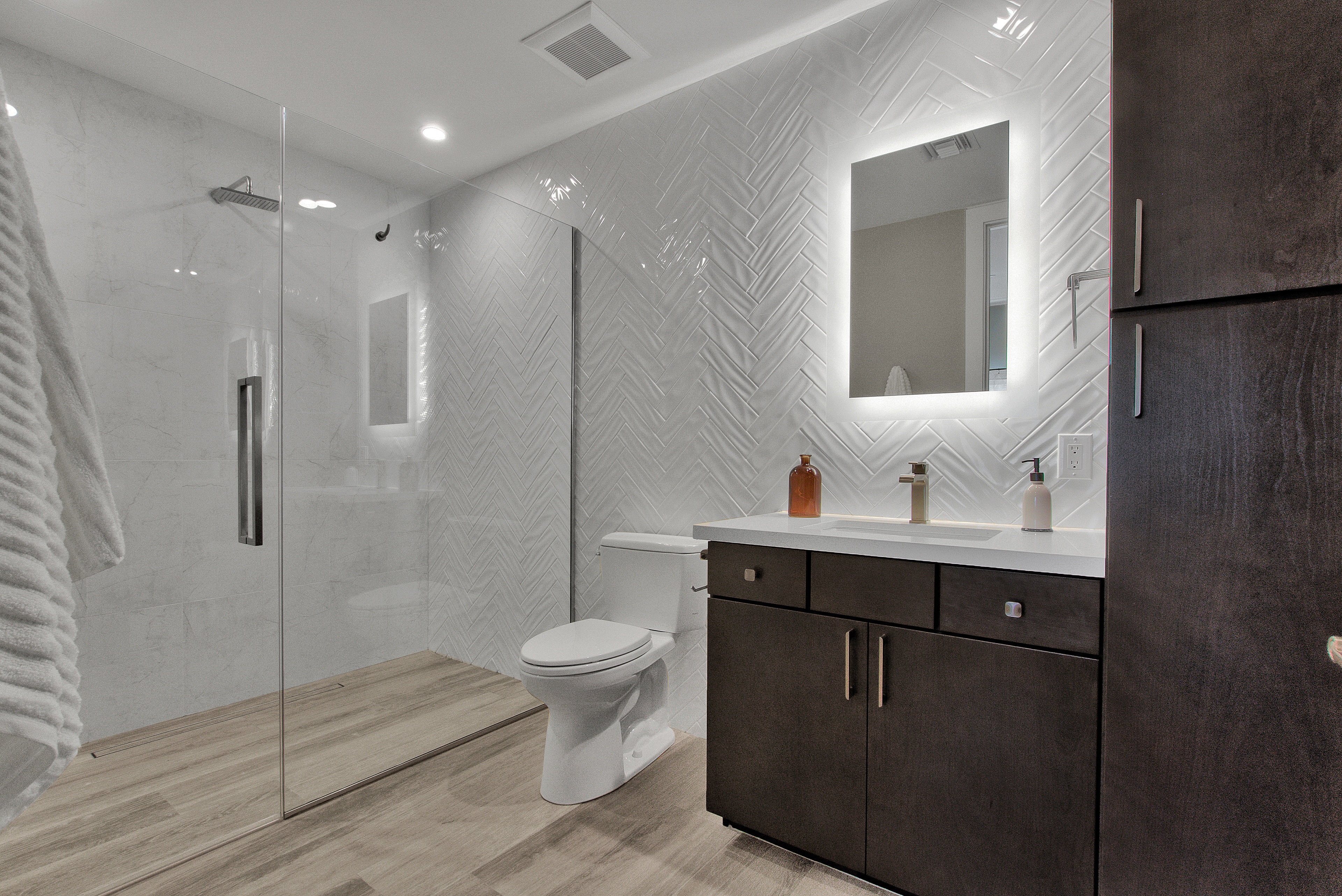 Home bathroom featuring mirror with spotlight lighting, dark toned hardwood cabinets, oak wood floors and a walk-in shower.